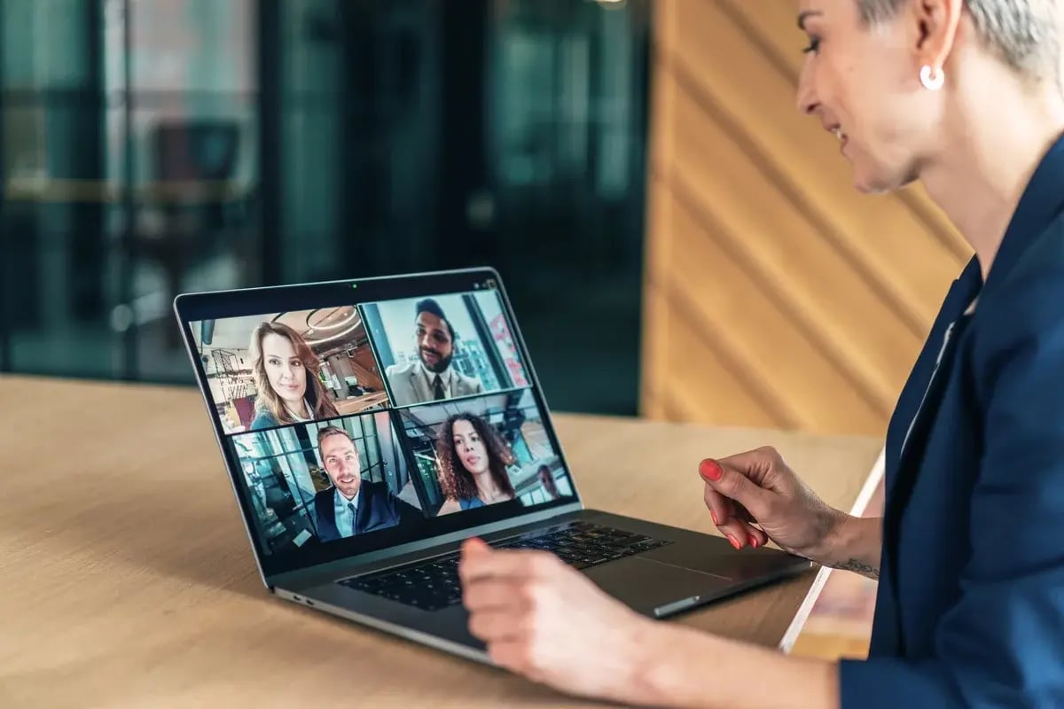 The image depicts a person sitting at a desk using a laptop for a video conference. The screen shows a video call with four participants, each in their own window. The person appears to be engaged in a virtual meeting, likely in a professional or casual setting. The image depicts a person sitting at a desk using a laptop for a video conference. The screen shows a video call with four participants, each in their own window. The person appears to be engaged in a virtual meeting, likely in a professional or casual setting.