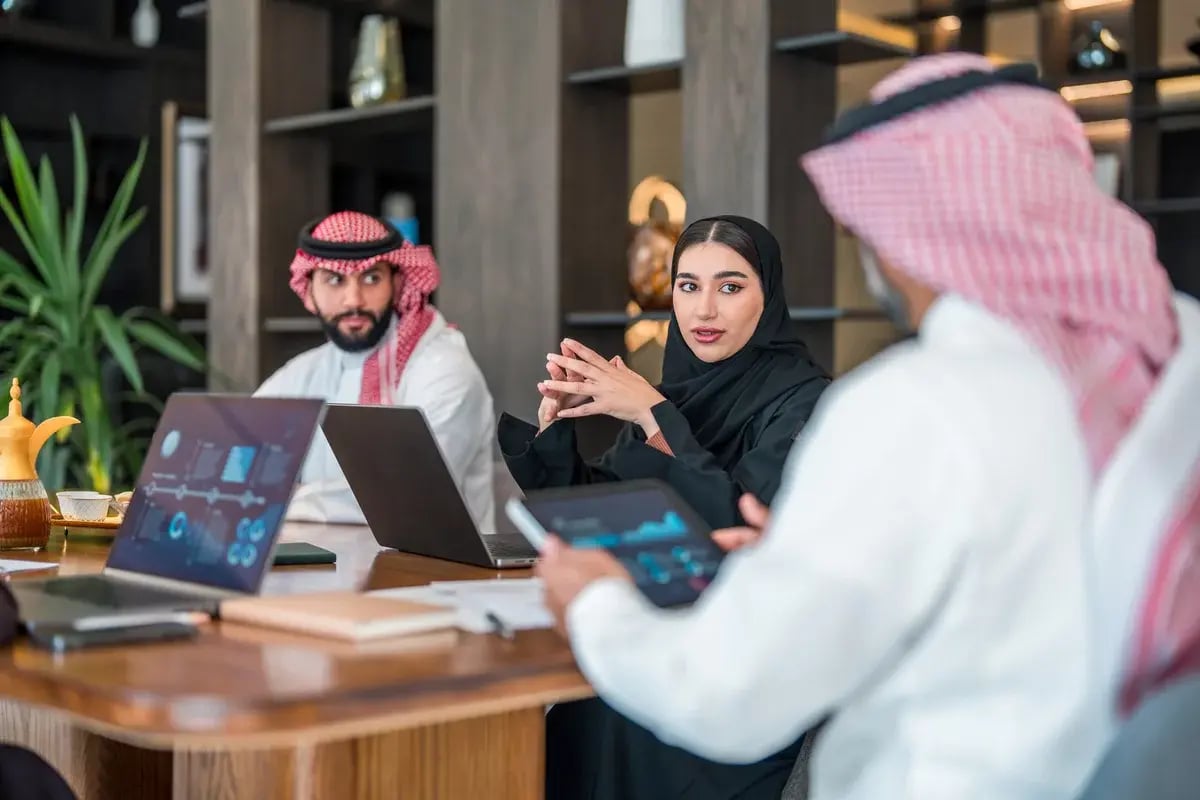 Diverse Arabic business executives discuss strategies at a meeting. The man wears traditional attire, while the woman is in a black abaya. Laptops and documents are present in a modern office setting, highlighting professional collaboration and analysis. Diverse Arabic business executives discuss strategies at a meeting. The man wears traditional attire, while the woman is in a black abaya. Laptops and documents are present in a modern office setting, highlighting professional collaboration and analysis.